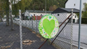 Foto av et grønt hjerte festet på et gjerde utenfor en skole.
