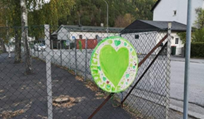 Foto av et grønt hjerte festet på et gjerde utenfor en skole.