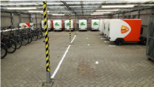 Foto fra innsiden til bylogistikkdepotet i Amsterdam. vi ser parkerte sykler og lastevogner til sykkel langs veggene.