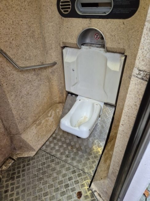 Bildet viser et toalett utenfor Stortinget hvor selve klosettet ikke ser ut som et vanlig klosset. Det har ikke toalett sete, spyleknapp eller vann. Toalettet befinner seg nede på gulvet, og det er ikke intuitivt hvordan man skal bruke det. Det er heller ingen toalettpapir eller vask.