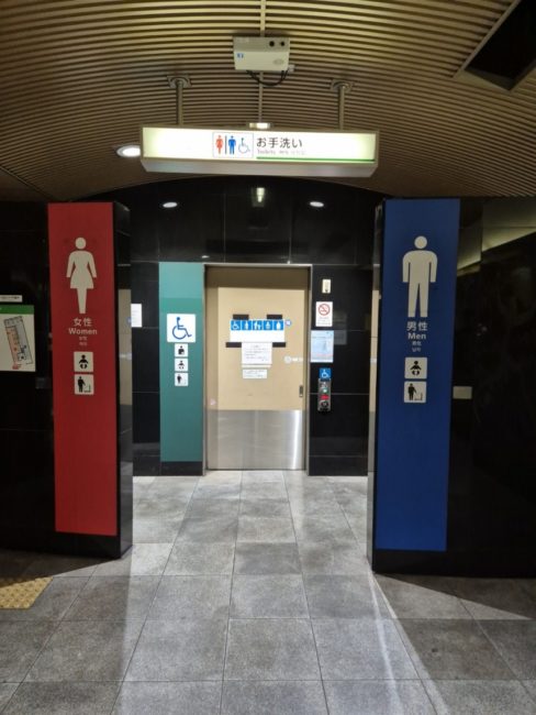 Bildet viser toaletter på en t-banestasjon i Japan. Skiltene ca. 40x200 cm høye og farget i rødt (dame) og blått (herre) og turkis (HC) slik at det er svært lett å få øye på dem også fra avstand.