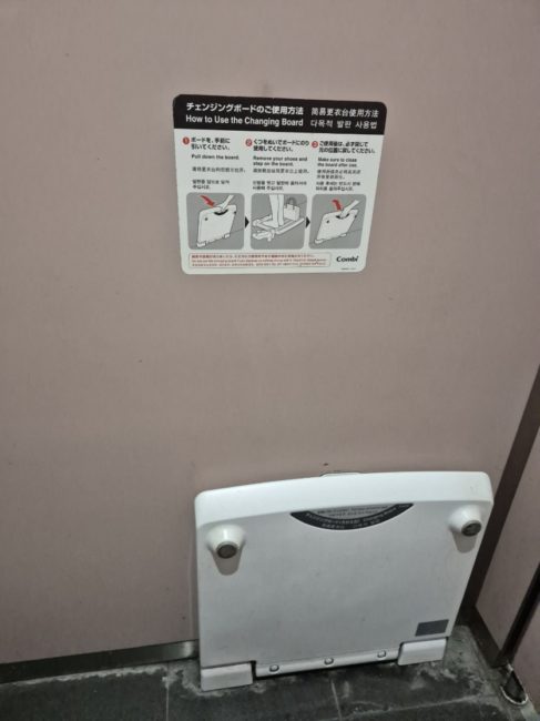 Bildet viser et toalett som har et brett festet på veggen. Brettet kan bøyes ned og brukes til å stå å skifte på dersom man har behov for dette.