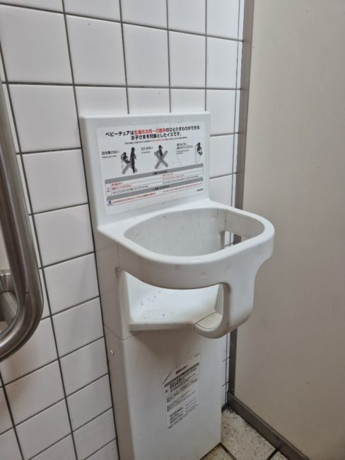 Bildet viser et offentlig toalett med en barnestol som er festet på veggen. Her er det mulig å sette fra seg barnet når man selv er på toalettet.